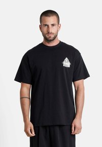 Zwarte katoenen t-shirt met een ronde hals, korte mouwen en een kleine witte grafische print op de linker borst. Classic fit.