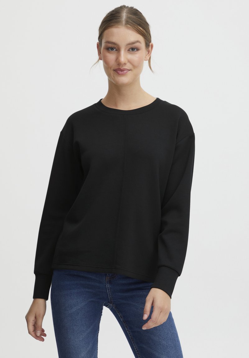 Schwarzes Rundhals Sweatshirt mit langen Ärmeln und lockerem Schnitt. Glatte Textur und sichtbare Nahtdetails. Kombiniert mit blauen Jeans.