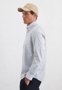 Striped long-sleeve shirt with a button-down collar, light blue and white stripes, and beige cap. Shirt features white buttons and a relaxed fit.