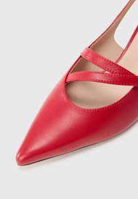 Rød skinnhøye hælersko med spiss tå, med kryssende stropper og et utskjæringsdesign for et særegent utseende.