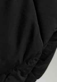 Czarna, pikowana kurtka z gładkim, matowym wykończeniem. Charakteryzuje się wyraźną, dopasowaną formą, przeszyciami i lekkim połyskiem na powierzchni.