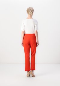 Rode op maat gemaakte broek met een cropped lengte en een rafelige zoom, gecombineerd met een eenvoudig wit t-shirt. Doorzichtige hakken maken de look af.