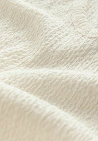 Texturiertes Creme-Gewebe mit einem welligen Muster, das eine weiche, leicht erhöhte Oberfläche und ein glattes, einladendes Erscheinungsbild aufweist.