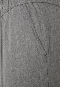 Szare spodnie dresowe z elastycznym paskiem w talii, z bocznymi kieszeniami i miękką fakturą. Materiał ma delikatny melanżowy wzór.