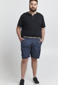Námornícke modré cargo šortky majú bočné vrecká, rolovaný lem a tkaný opasok. Skombinované s čiernym tričkom s krátkym rukávom a gombíkmi.