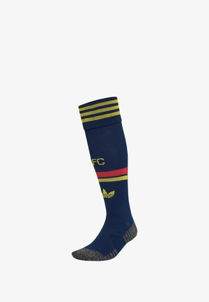Calcetín alto azul marino con rayas amarillas y rojas, letras amarillas AFC, logo amarillo de Adidas y áreas grises texturizadas en la puntera y el talón.