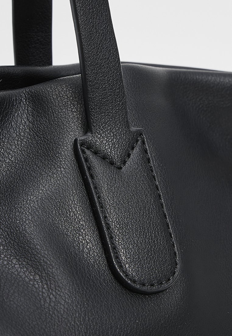 Nahaufnahme einer schwarzen Ledertasche, die die strukturierte Oberfläche und die genähten Riemenbefestigungen mit glatten Kanten zeigt.