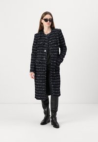 Marinblå tweedjacka med texturerad finish, långa ärmar och framfickor. Kombinerad med figurnära svarta byxor och knähöga svarta stövlar.
