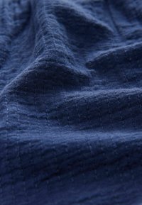 Tissu texturé bleu marine avec un motif en grille, présentant une texture tissée douce et un éclat subtil, plié en vagues douces.