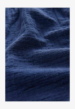 Sötétkék texturált szövet, rácsos mintával, puha, szőtt textúrával és enyhe fénylésével, lágy hullámokba hajtva.