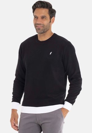 Sweat-shirt noir à manches longues, col rond, avec poignets et ourlet côtelés blancs. Présente un petit logo sur la poitrine. Texture de tissu doux.