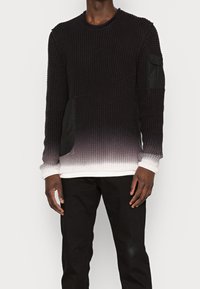 Pull en maille noire avec un effet ombragé se dégradant en blanc à l'ourlet. Présente des patches en tissu noir sur les côtés et les manches.