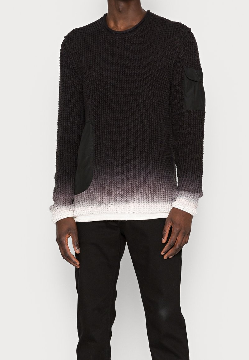 Pull en maille noire avec un effet ombragé se dégradant en blanc à l'ourlet. Présente des patches en tissu noir sur les côtés et les manches.