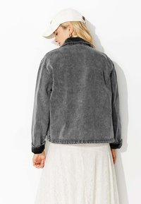 Veste en velours côtelé gris à coupe décontractée, avec un col classique et des poignets, présentée sur une jupe blanche en dentelle.