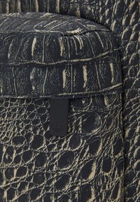 Texturerad tygväska i mörk marin med ett ljusbeige sprickmönster. Har en svart varumärkesetikett och en vadderad topp för stöd.