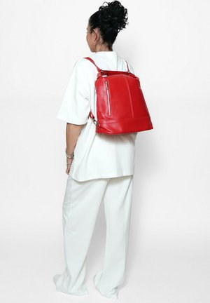Zaino in pelle rossa con due spalline regolabili, una maniglia superiore e due tasche anteriori con zip. Texture liscia e design strutturato.