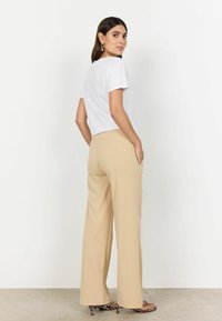 Relaxed-fit white cotton t-shirt with short sleeves paired with beige wide-leg trousers featuring side pockets, worn with animal print heeled sandals.