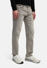 Light gray denim jeans with a straight fit, detailed stitching, five pockets, and a black label at the waistband, paired with white sneakers.