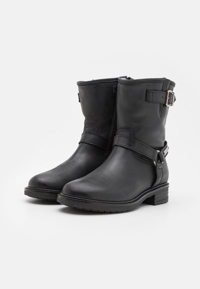 Botines de cuero negro hasta el tobillo con punta redondeada, correa ajustable con hebilla, laterales texturizados y tacón bajo en bloque. Acabado suave con costuras visibles.