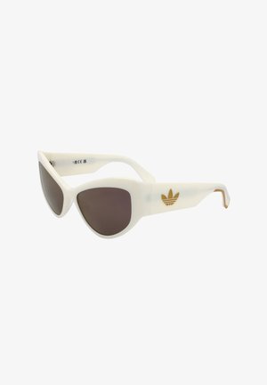 Occhiali da sole bianchi a forma di occhio di gatto con lenti scure e logo Adidas dorato sulle aste, mostrati su sfondo bianco.