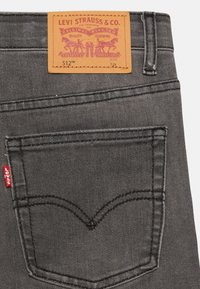 Čierne denimové džínsy s prešitým zadným vreckom a červenou nášivkou Levi's. Obsahujú hnedú koženú nálepku s informáciami o značke. Klasický strih, odolný materiál.