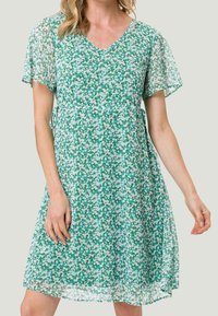 Vestido verde con escote en V y mangas cortas con volantes. Hecho de una tela ligera con un patrón de flores blancas y azul claro dispersas.