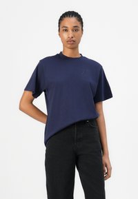 Tricou din bumbac de culoare bleumarin, cu mâneci scurte, având un mic logo brodat pe piept, asortat cu blugi negri din denim.
