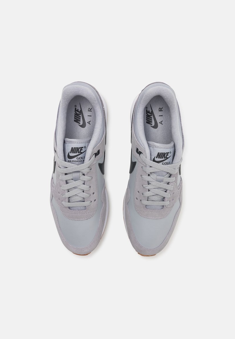 Les baskets Nike Air Pegasus 83 présentent une tige gris clair avec des accents en suède, un logo Swoosh noir, des lacets gris et une semelle extérieure en caoutchouc marron.