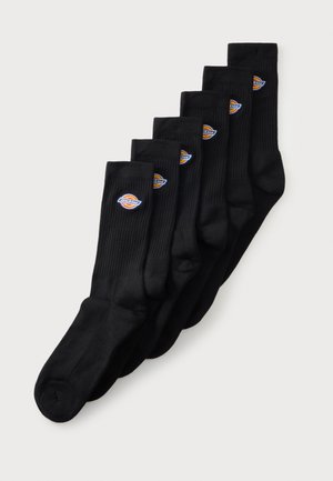 Seis pares de calcetines negros hasta media pantorrilla con textura acanalada, cada uno con un pequeño parche redondo multicolor con el logo cerca de la parte superior.