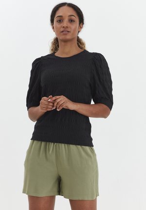 Sort tekstureret top med pufærmer, parret med lyse olivengrønne shorts. Toppen har en rund halsudskæring og et subtilt mønster.
