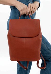 Brauner Leder-Rucksack mit strukturierter Oberfläche, Klappenverschluss und verstellbaren Schultergurten. Einfarbig, minimale Hardware-Details.