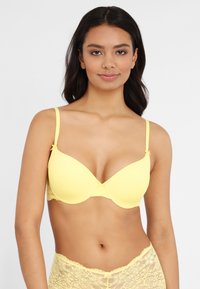 Yellow padded bra with lace details at the sides and back, adjustable straps, and a small bow accent at the center. Smooth texture overall.
