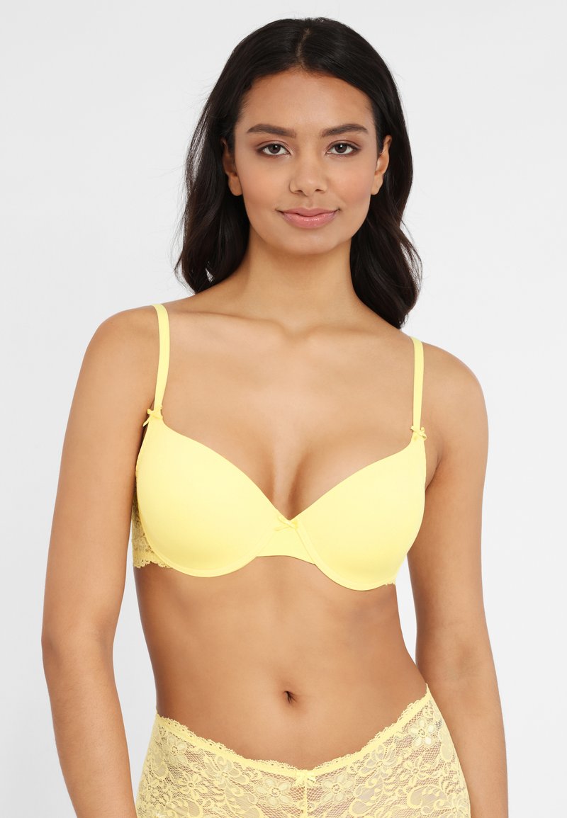 Yellow padded bra with lace details at the sides and back, adjustable straps, and a small bow accent at the center. Smooth texture overall.