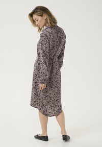 Langarmige jurk met een bloemenpatroon in tinten van roze en zwart. Heeft een strik in de taille en een gebogen zoom, gecombineerd met zwarte instappers.