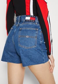 Světle modré džínové kraťasy s ohrnutým lemem, se dvěma zadními kapsami a značkovou nášivkou s nápisem "TOMMY JEANS" na pásku.