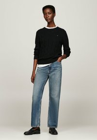 Pull en maille noir avec un ourlet côtelé, associé à un jean droit bleu clair et des mocassins noirs, avec un t-shirt blanc à col rond en dessous.