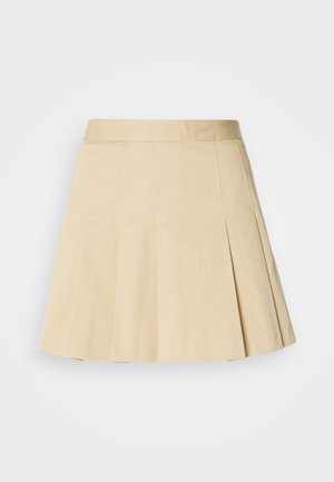 Gonna plissettata in cotone beige chiaro, con una vita e quattro cuciture verticali nella parte anteriore. L'orlo è leggermente svasato per favorire il movimento.