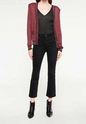 Cardigan tricoté rouge avec un motif texturé, top noir à col en V et jeans noirs évasés, associés à des bottines noires.