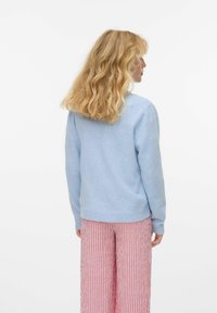 Pull bleu clair avec un col rond et des poignets côtelés, associé à un pantalon à jambes larges à rayures rouges et blanches. Texture douce et coupe décontractée.