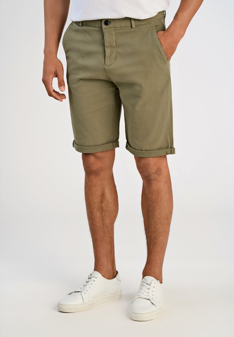 Olivgrüne Shorts aus strapazierfähigem Stoff mit geradem Schnitt, umgeschlagenen Säumen und Fronttaschen, kombiniert mit weißen Sneakers.