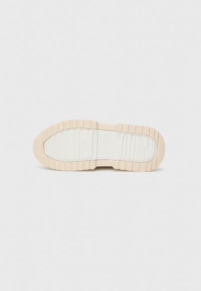Suela de zapato en beige con una superficie texturizada y acanalada. Entresuela blanca y clara. El diseño presenta una punta redondeada y bordes de goma prominentes y gruesos.
