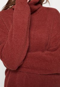 Svetr v měděné barvě s designem roláku, vyrobený z měkkého, chlupatého materiálu. Má volné rukávy a uvolněný střih.