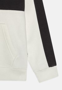Sudadera con capucha en negro y crema con un diseño a bloques de color, que cuenta con un bolsillo frontal, puños acanalados y una textura de tela suave.