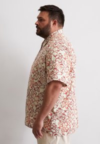 Chemise à manches courtes avec un fond crème et un imprimé floral rouge, en tissu léger et à la coupe décontractée.
