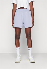 Světlofialové sportovní kraťasy s elastickým pasem, doplněné bílými ponožkami po kotníky a světlými teniskami, zepředu.