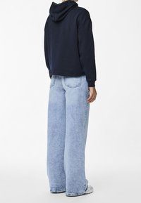 Marinblå kort hoodie med huva, matchad med ljusblå vida jeans som har en bleknad textur och synliga sömnadsdetaljer.