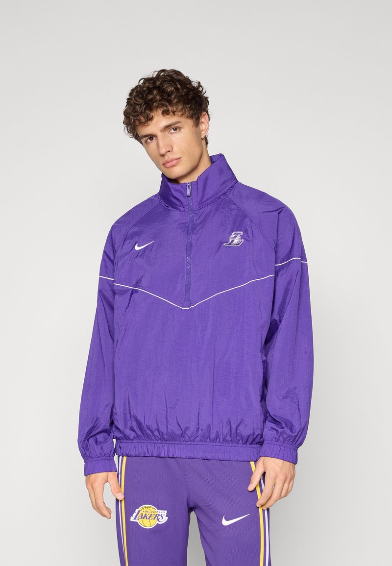 Lila nylon pulóverdzseki magas gallérral, cipzáras elülső résszel és fehér díszvarrással. A Lakers logójával és rugalmas mandzsettával rendelkezik.