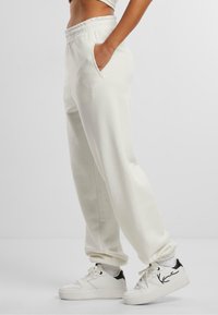 Hvide fleece sweatpants med elastisk talje, sidelommer og ribbede manchetter, parret med hvide sneakers med sorte accenter.