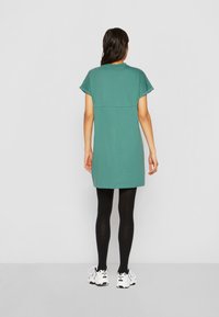 Teal bomulls kjole med korte ermer, løs passform, over-kneet lengde, kombinert med svarte leggings og hvite joggesko.