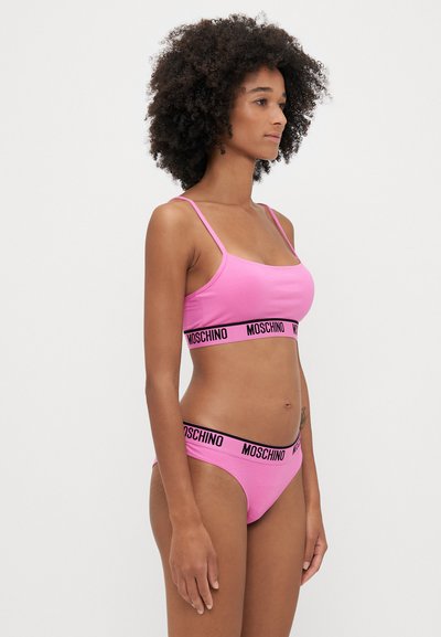 Rózsaszín pamut fehérnemű szett, amely egy vékony pántos bralette-ből és egy hozzá illő bikini alsóból áll, mindkettő a fekete "MOSCHINO" logós pánttal díszítve.